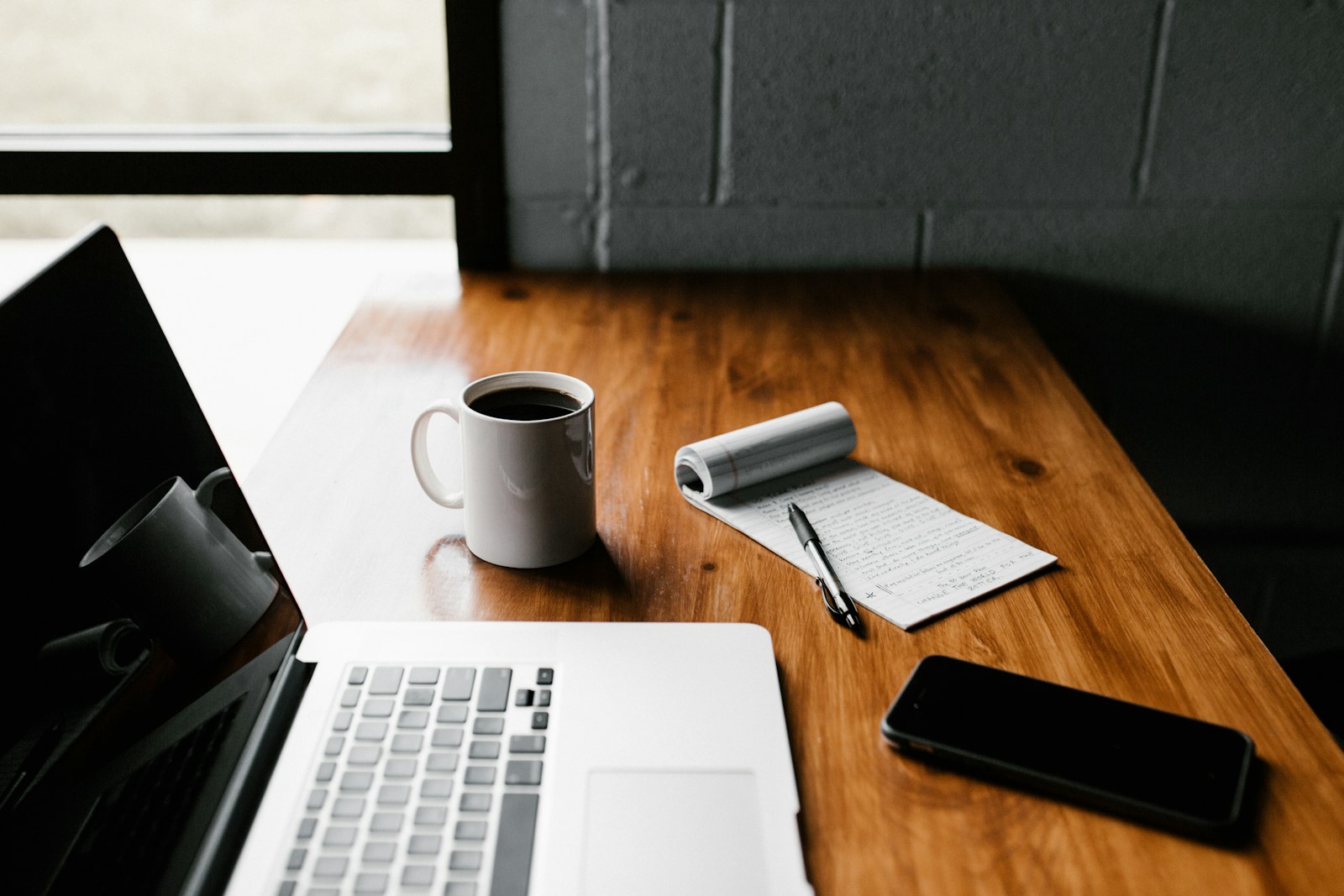 Mesa de trabajo con portátil, taza de café y libreta abierta con notas escritas a mano